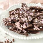 A white plate with pile of dark chocolate and pink bark pieces. Light pink background.