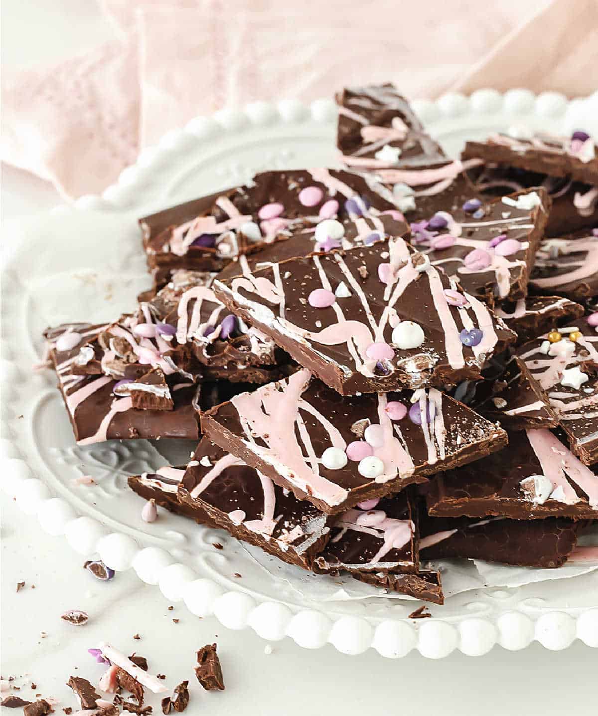 Pile of dark chocolate and pink bark pieces on a white plate. Light pink background.