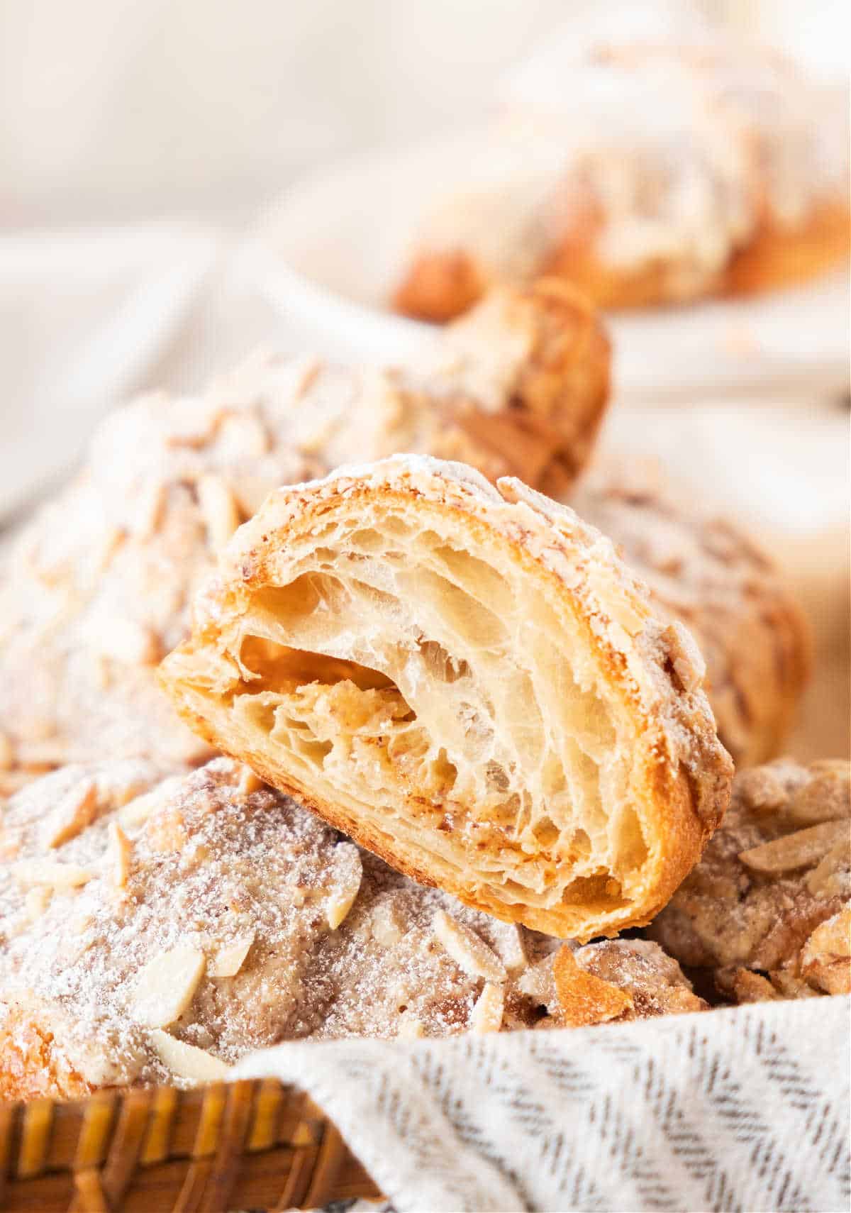 Half almond croissant on a pile of whole ones. Striped cloth, greyish white background. 