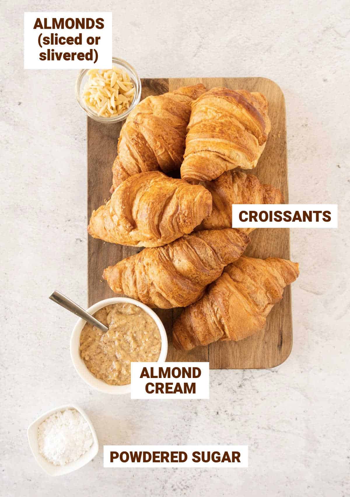 Light gray surface with croissants, almonds, almonds cream on a wooden board.