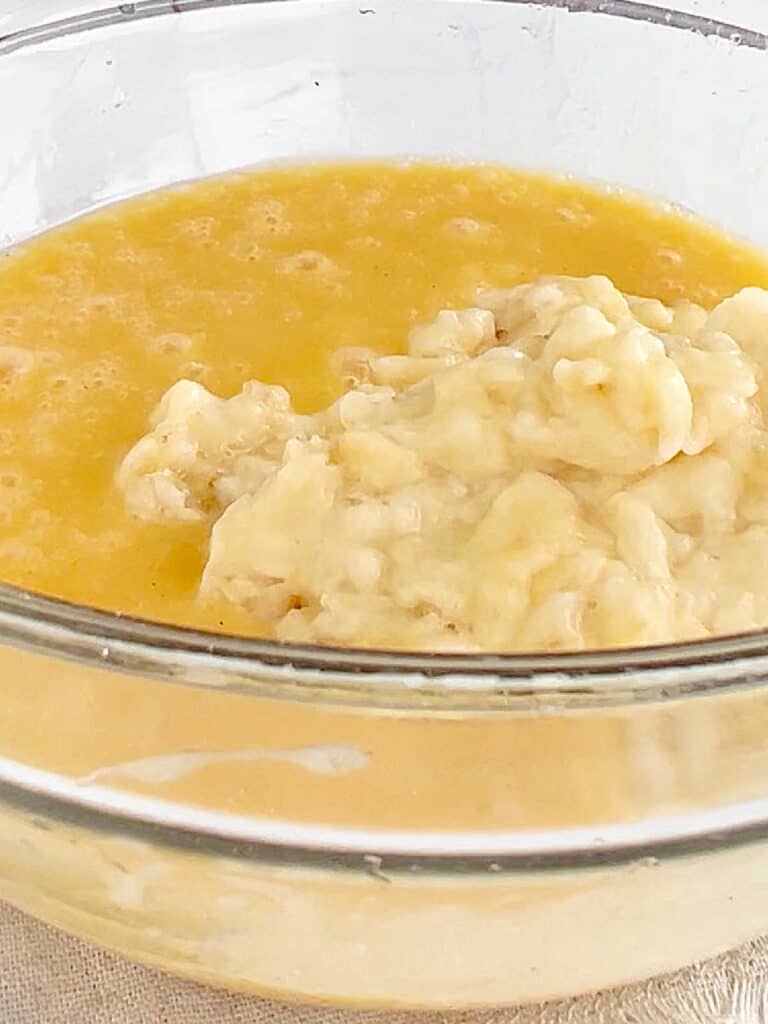 Mashed banana added to muffin batter in a glass bowl.