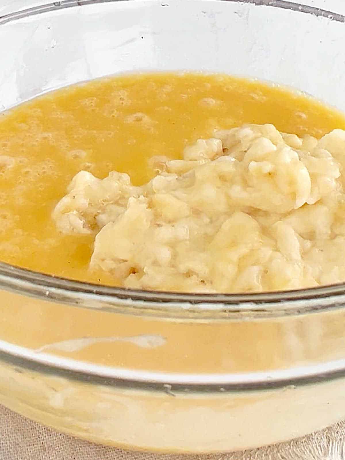 Mashed banana added to muffin batter in a glass bowl.