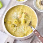 Broccoli cheddar soup in a white bowl with a spoon on a grey wooden board.