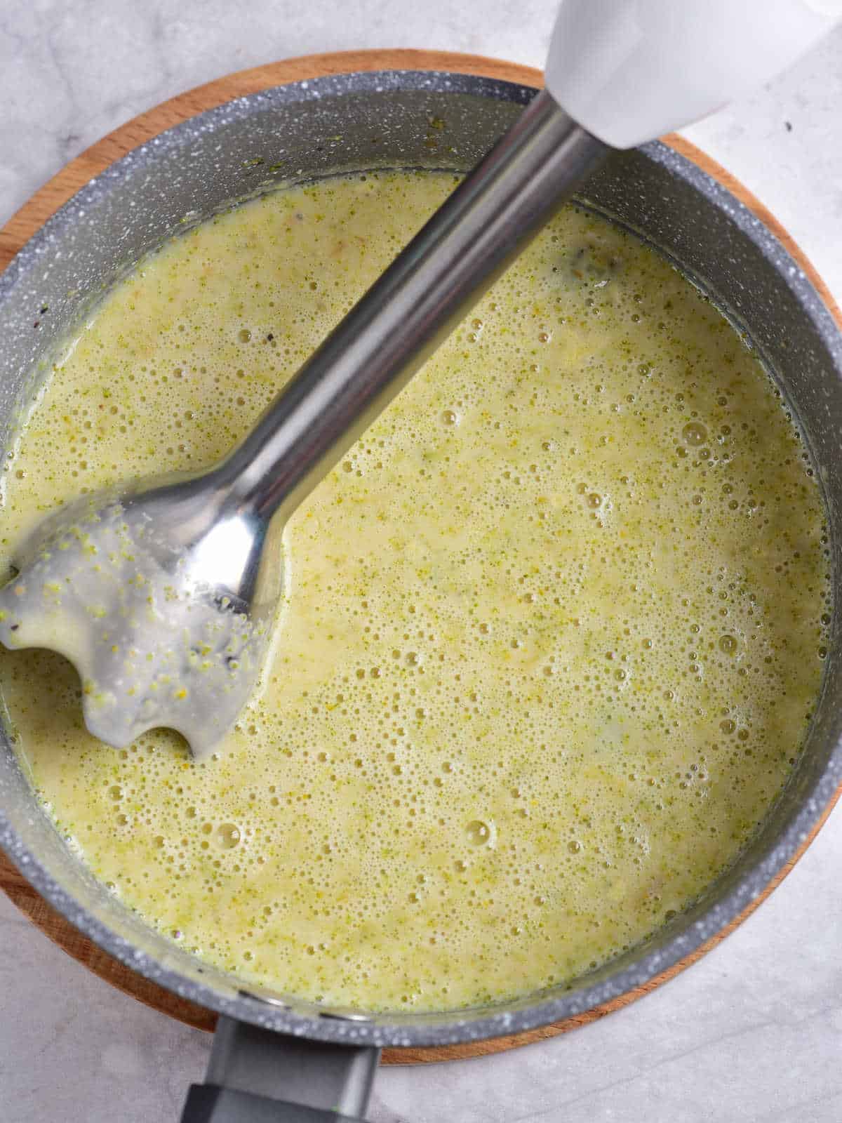 Immersion blender inside a gray pot with blended broccoli soup. 