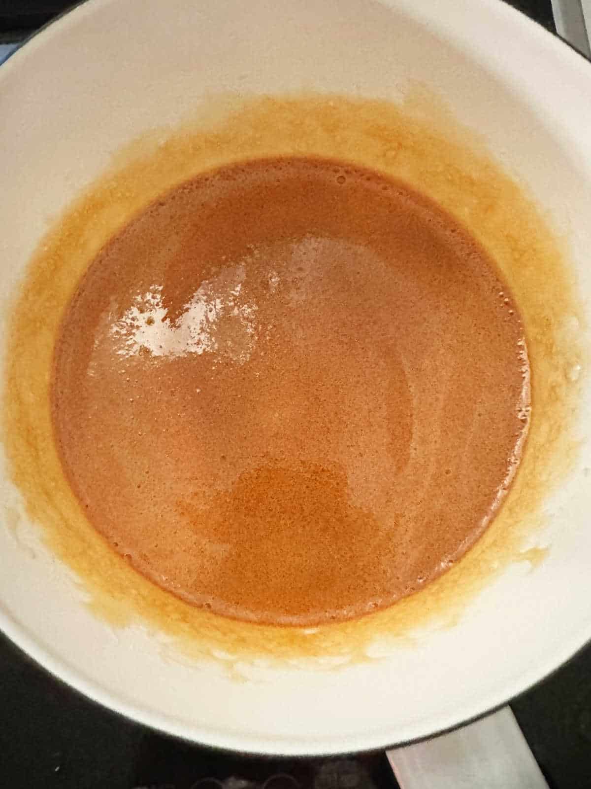 Amber colored caramel in a white saucepan. Top view.