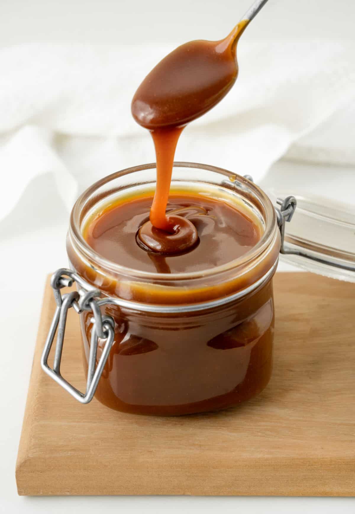 Homemade caramel being spooned from a mason jar on a wooden board. White background. 