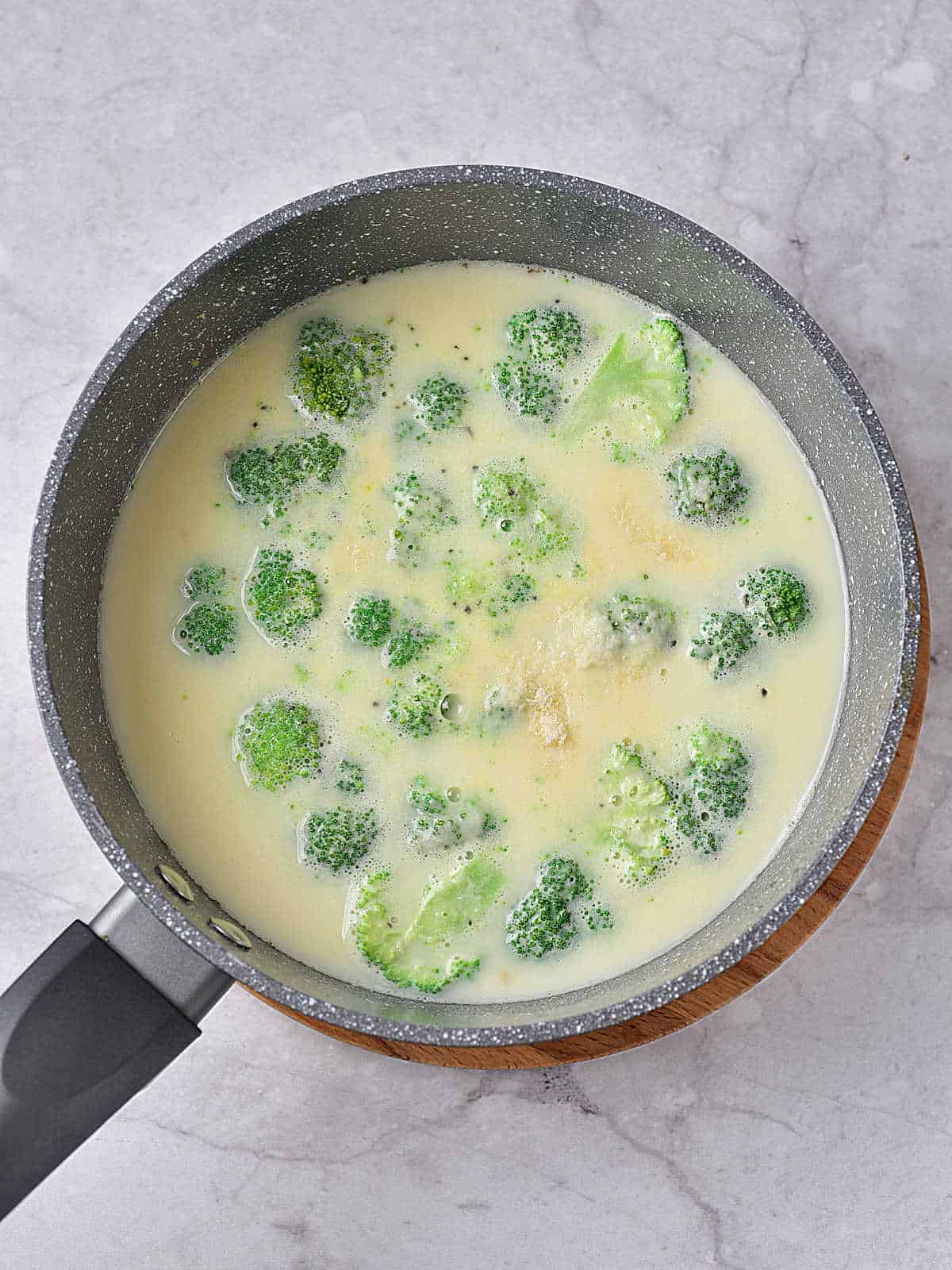 Gray saucepan with soup and broccoli florets on a gray surface.