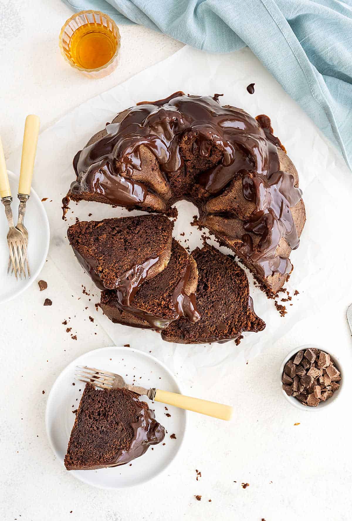 Top view of chocolate glazed chocolate bundt cake. White surface, few cut slices, forks.