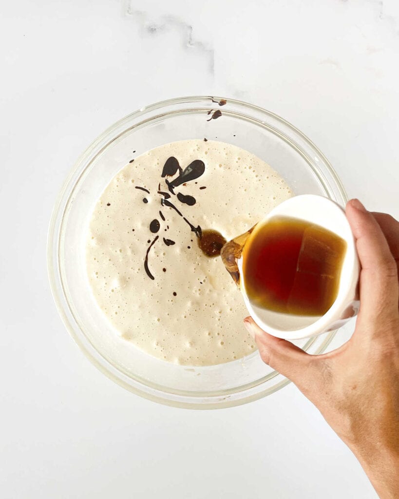 Adding bourbon to whipped eggs and sugar in a glass bowl. White surface.