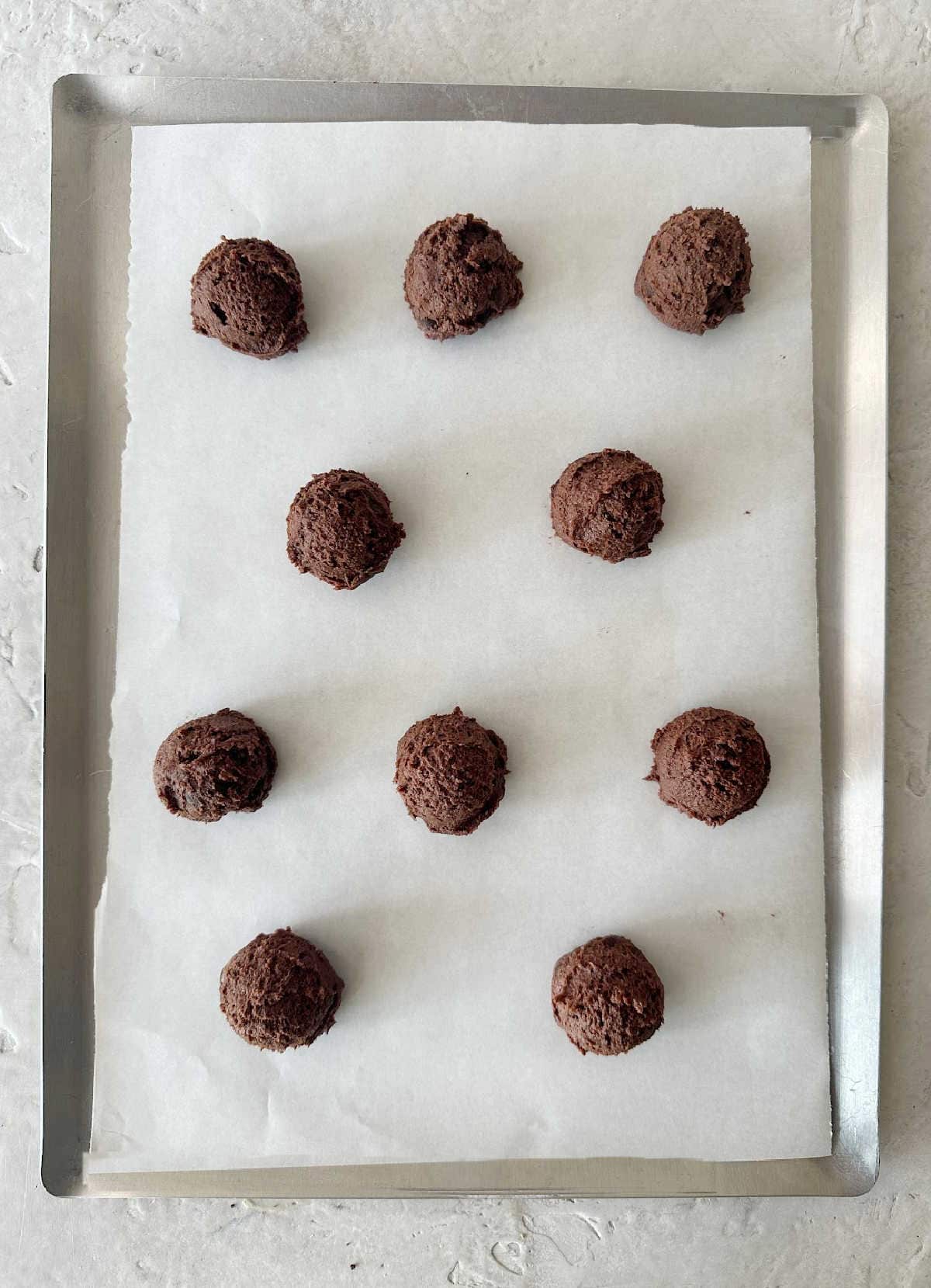 Metal pan with parchment paper and chocolate cookies before baking.