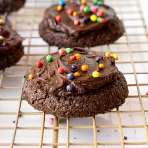 Wire rack with frosted chocolate cookies with colorful sprinkles.