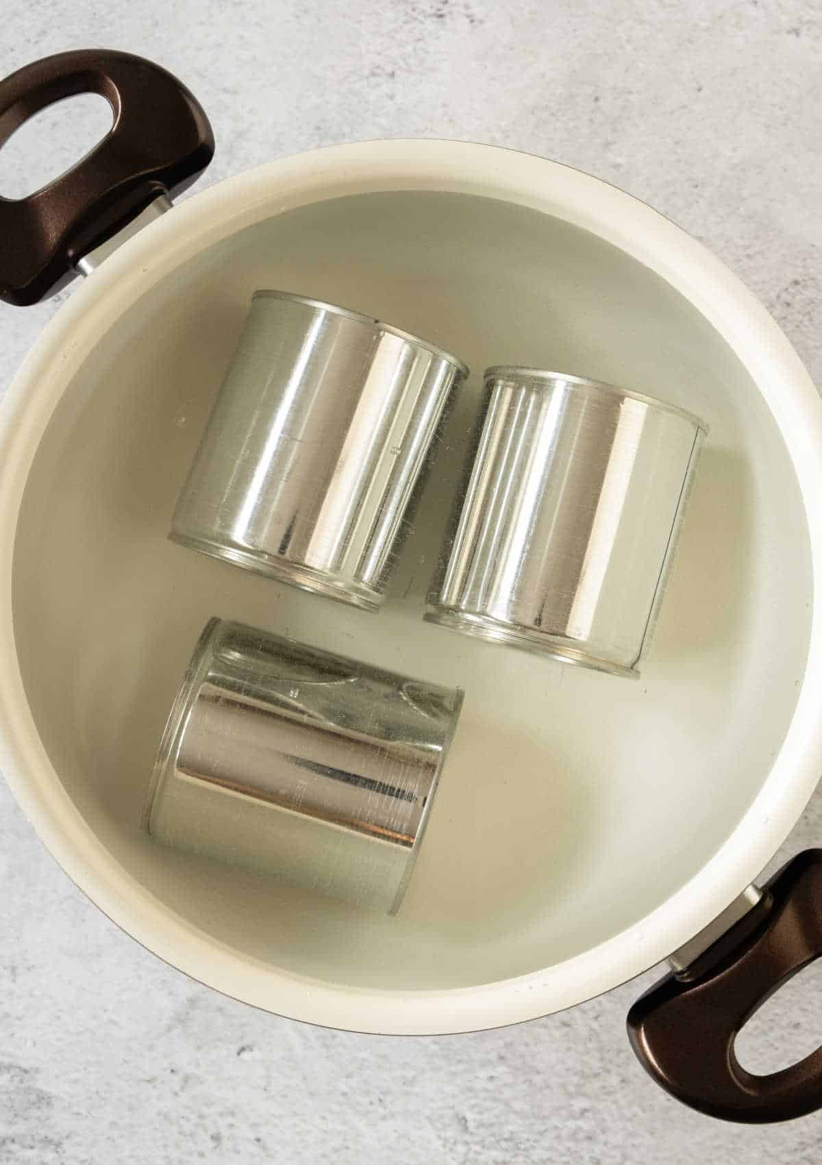 Large white pot with water and three metal cans. Light gray surface.