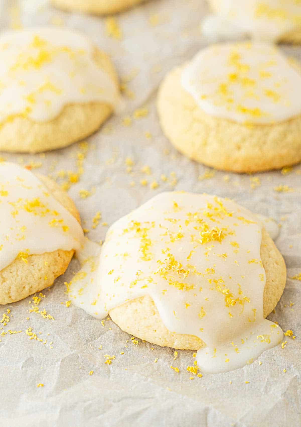 Softly glazed ricotta cookies with lemon zest on top. Gray surface.