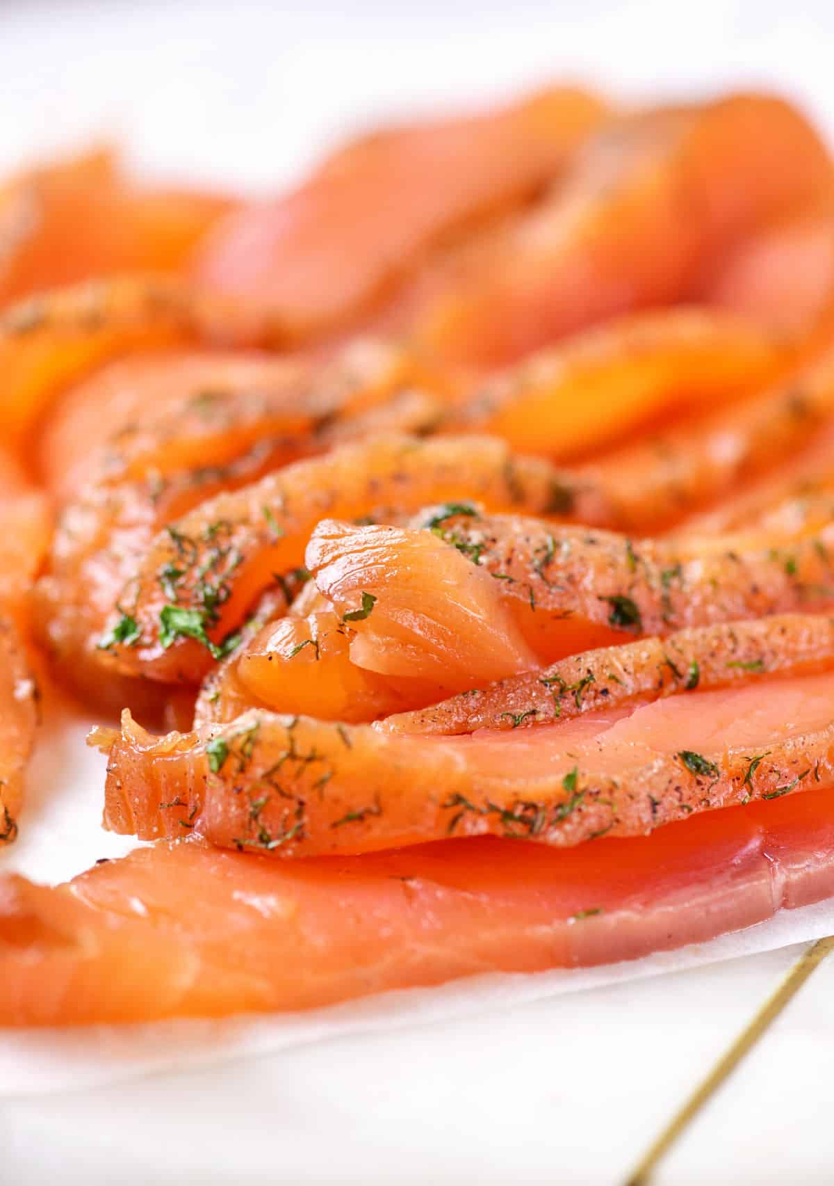 Close up of homemade gravlax with dill crust on a white plate.