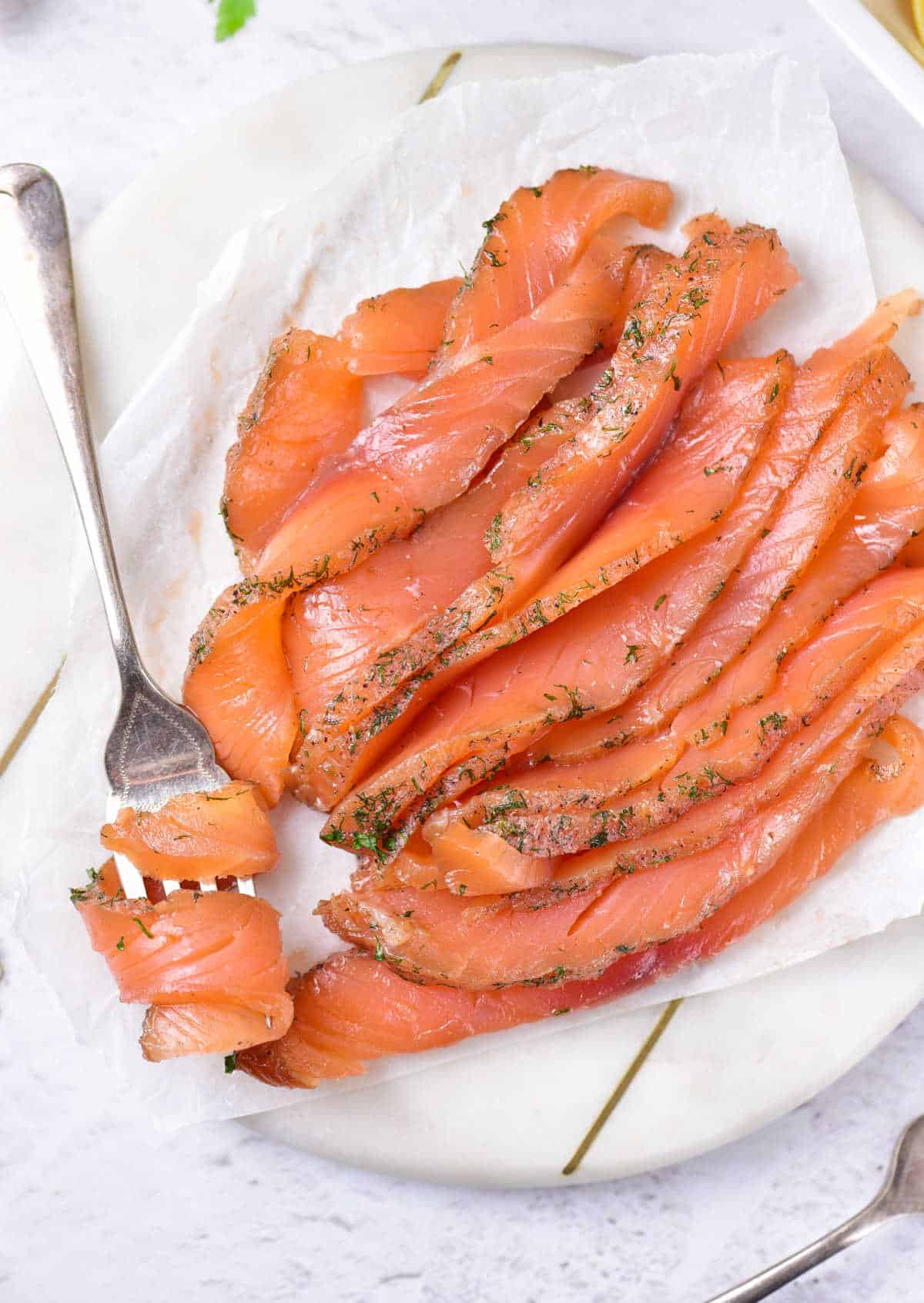 Slices of gravlax on a white plate with silver fork. White surface. 