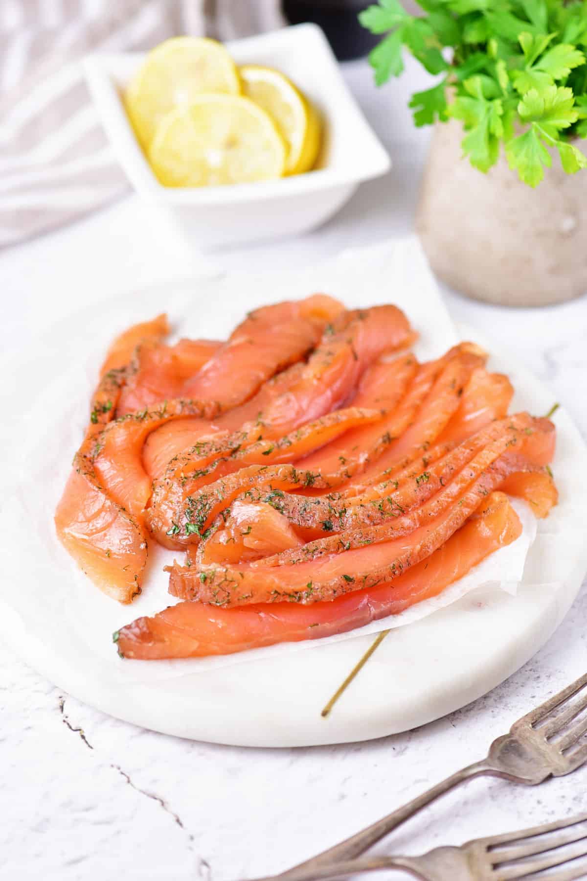 Sliced cured salmon with dill on a white plate. Lemon and herbs on the white background.