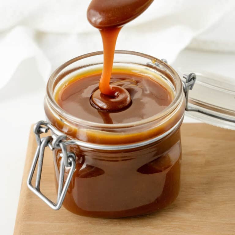 Caramel sauce in a mason jar on a wooden board. White background.