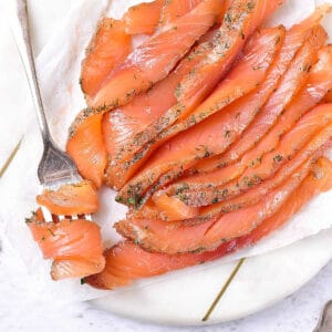 White plate of dill-crusted cured salmon with a silver fork.