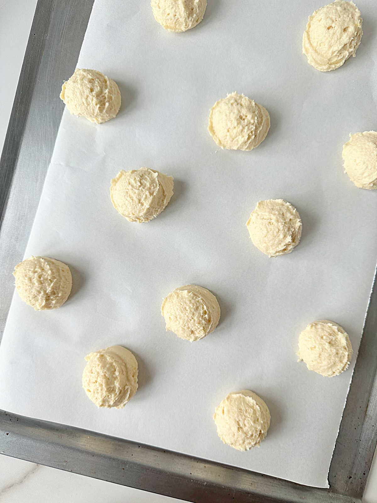 White parchment paper with ricotta cookies before baking on a metal tray.