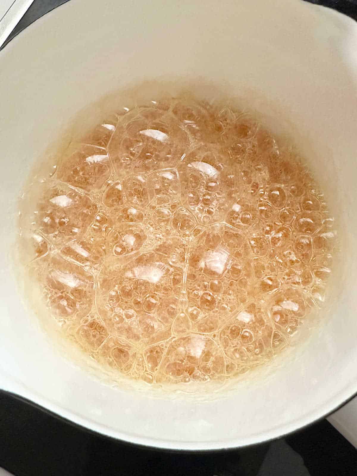 Large light amber color bubbles in a white saucepan.