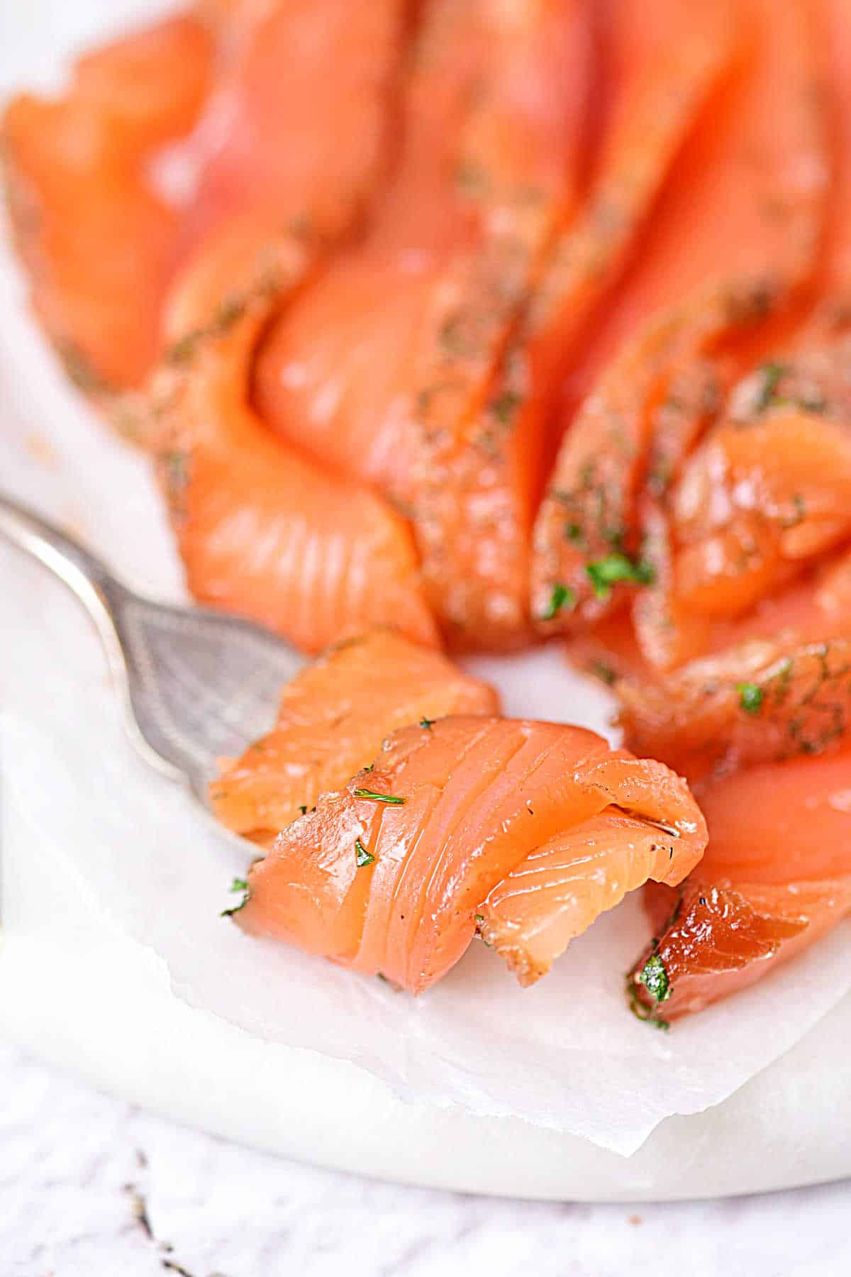 Bite of smoked salmon wrapped on a silver fork on a white plate with more salmon.