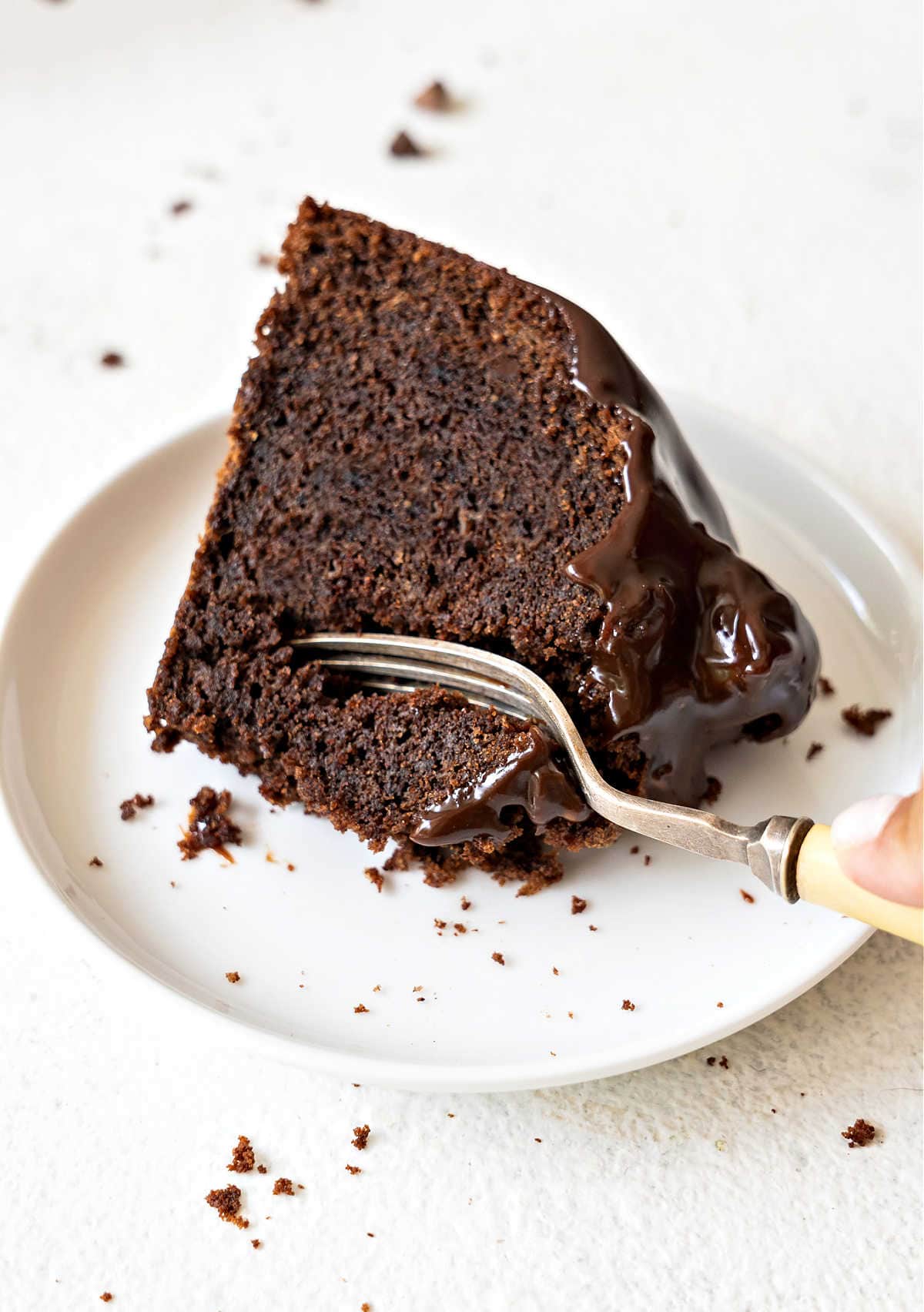 Forking a slice of glazed chocolate bundt cake on a white plate. White background.