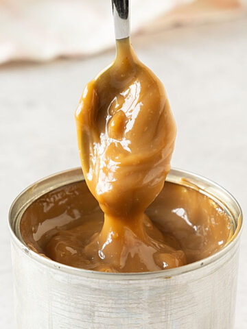 Spooning dulce de leche from a metal can on a light gray surface.