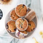 Close up of blueberry banana muffins in white paper liners. White surface, light blue cloth.