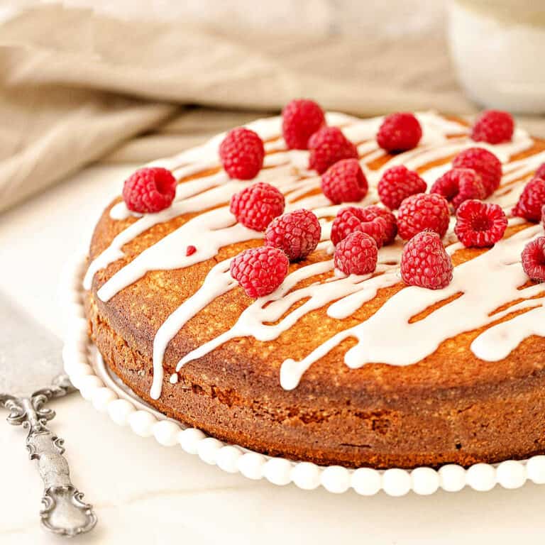 Raspberry coffee cake with glaze and fresh berries on a white plate. White surface, beige background.