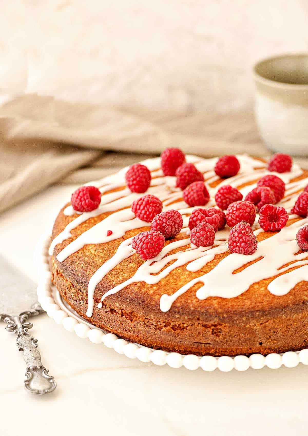 Raspberry topped glazed round coffee cake. White surface, beige background.