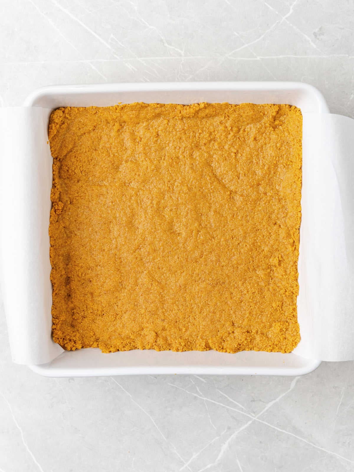 Baked graham cracker crust in a white ceramic pan on a light gray surface.