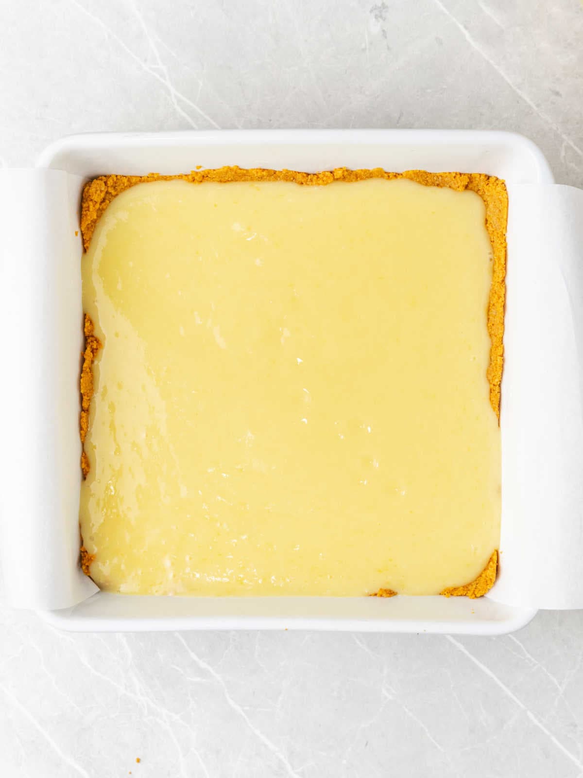 Unbaked lemon bars in a white pan with parchment paper. Light gray surface.