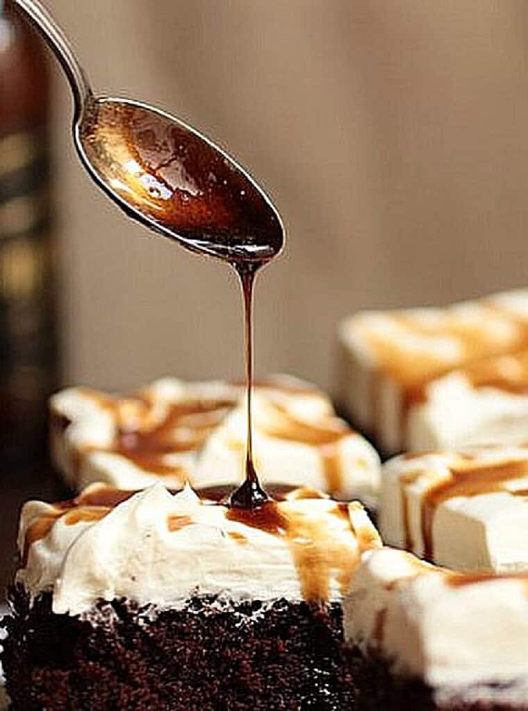 Guinness berr syrup dripping from a spoon onto chocolate cream cake squares.