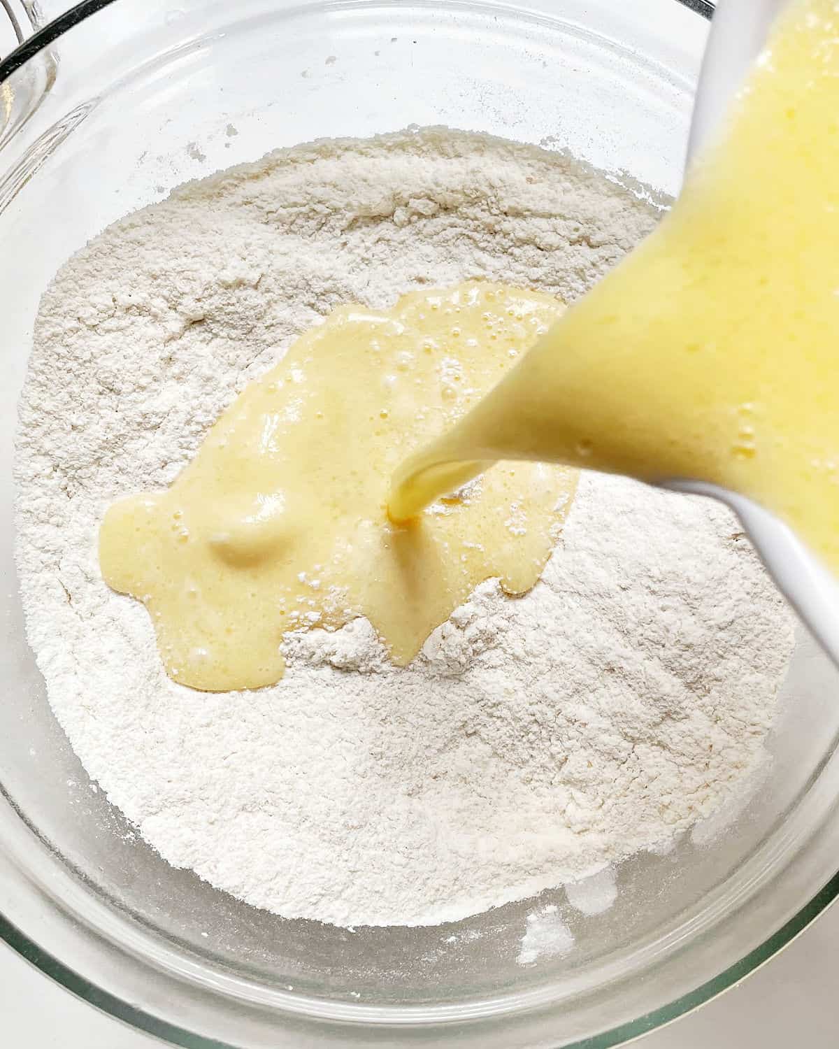 Adding wet muffin ingredients to dry ingredients in a glass bowl.