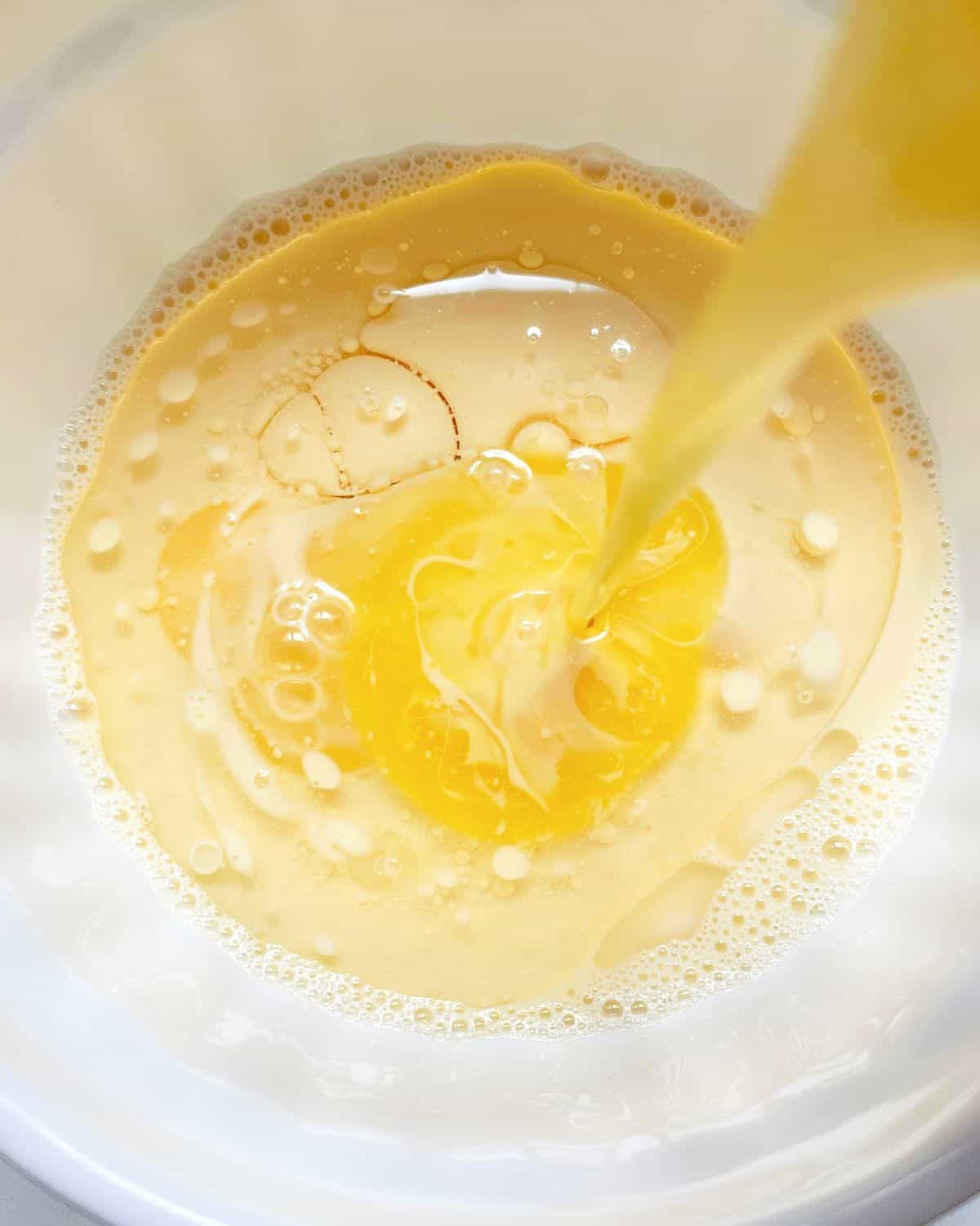 Adding melted butter to oil and milk in a white bowl.