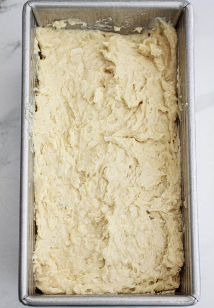 Metal pan with coconut pineapple bread batter. White surface.
