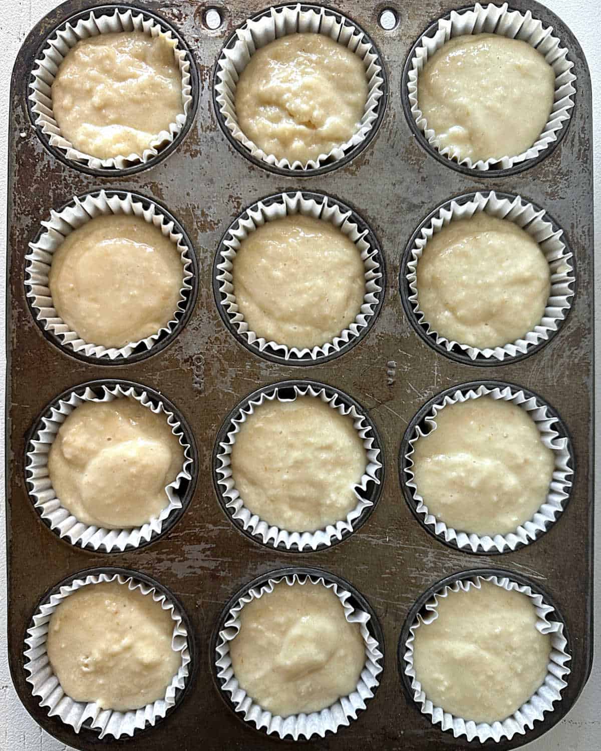 Muffin pan with twelve coconut muffins in paper liners before baking.