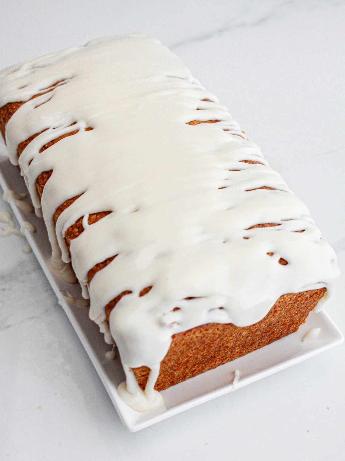 Loaf cake with glaze on a white dish. White marbled surface.