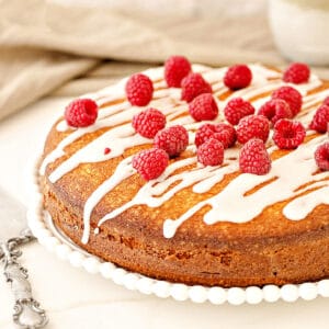 Raspberry coffee cake with glaze and fresh berries on a white plate. White surface, beige background.