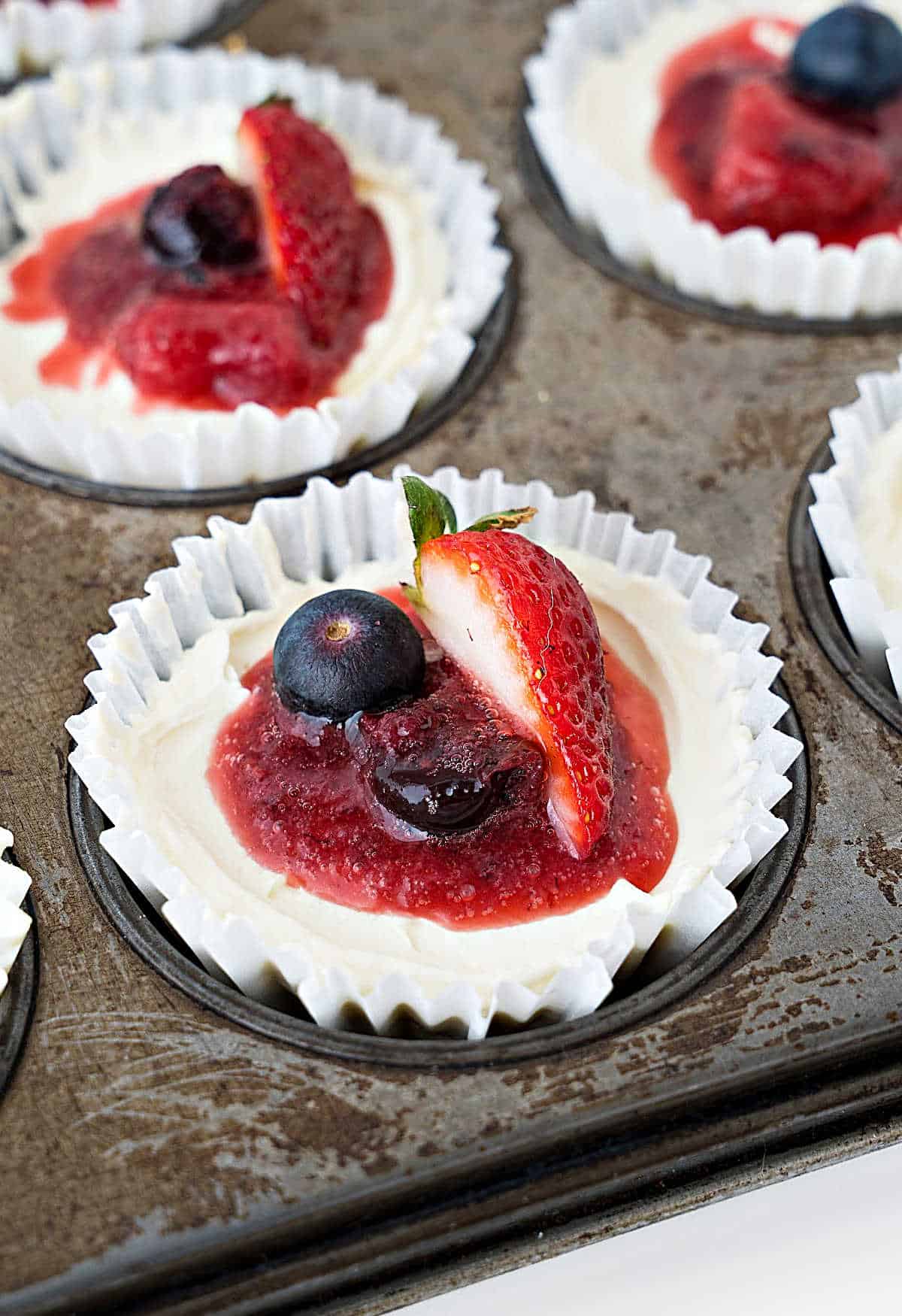 Close up white paper liner with berry mini cheesecakes in a metal muffin pan.