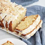 Close up of blue cloth with white tray of glazed coconut bread with almond topping.
