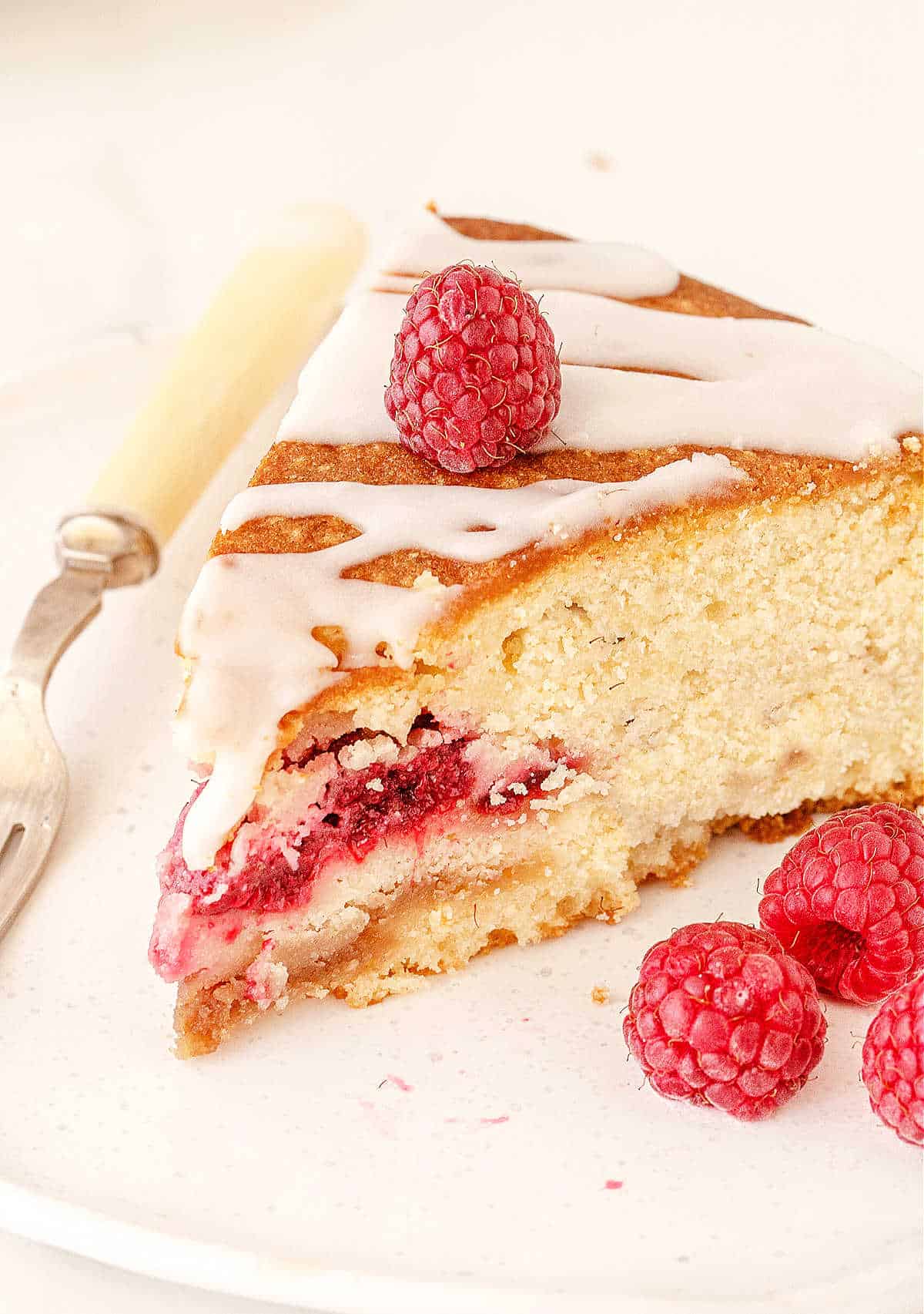 Glazed raspberry coffee cake slice on a white plate with fork. Fresh berries.