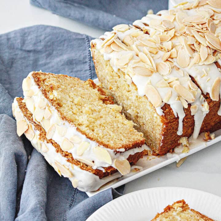 Close up of blue cloth with white tray of glazed coconut bread with almond topping.