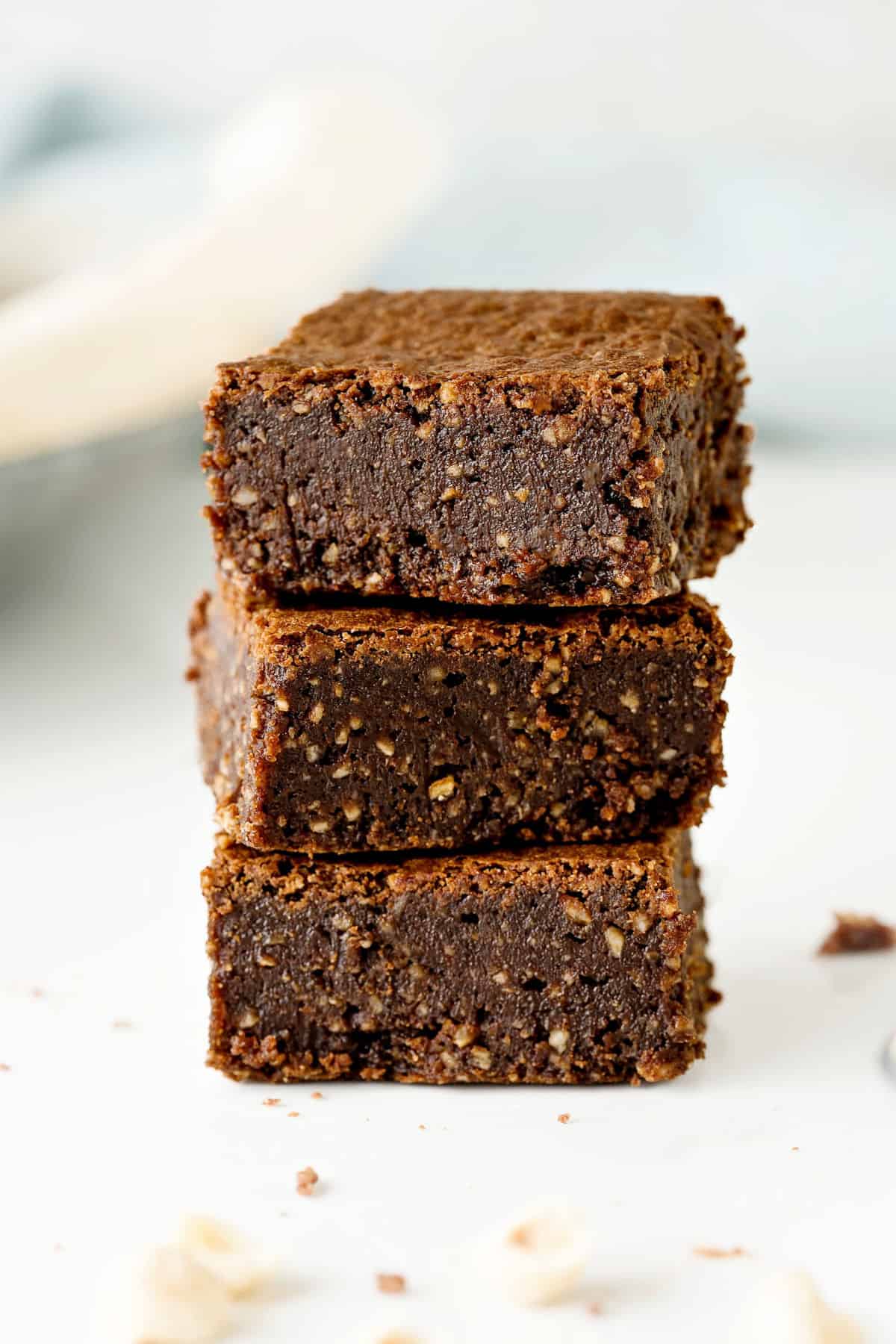 Three gluten-free hazelnut brownies stacked on a white surface.
