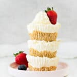 Light gray background with stack of three mini cheesecakes on a pink plate. Berries. White surface.