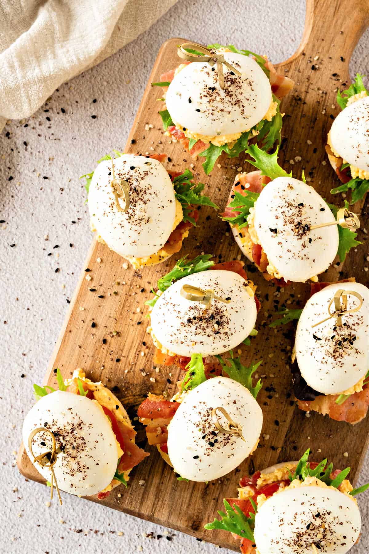 Top view of wooden board with BLT deviled egg sandwiches. Light gray surface.