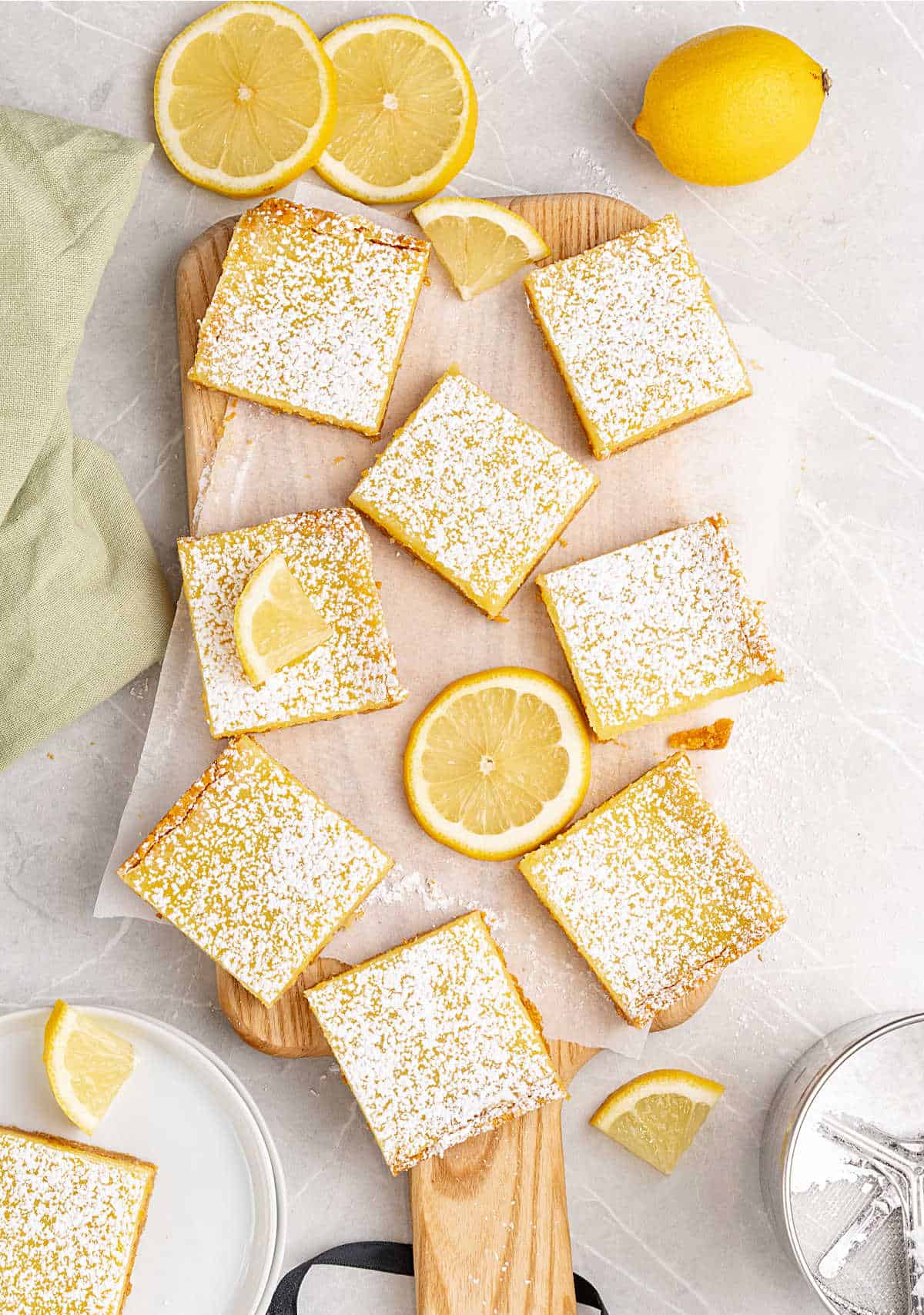Top view of powdered sugar covered lemon bars on a wooden board. Light gray surface.