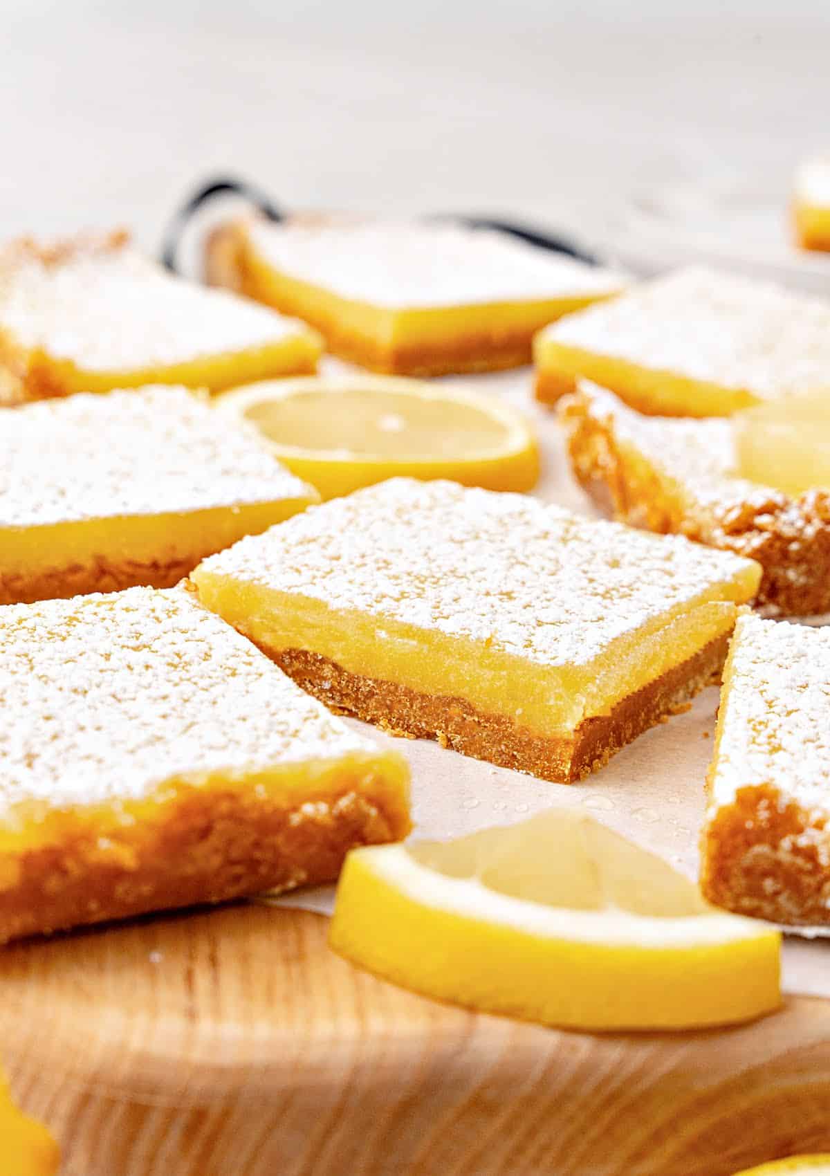 Wooden board with several lemon bars with powdered sugar. Light gray background.