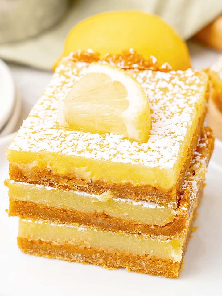 White plate with three lemon squares in a stack. Lemon slices.