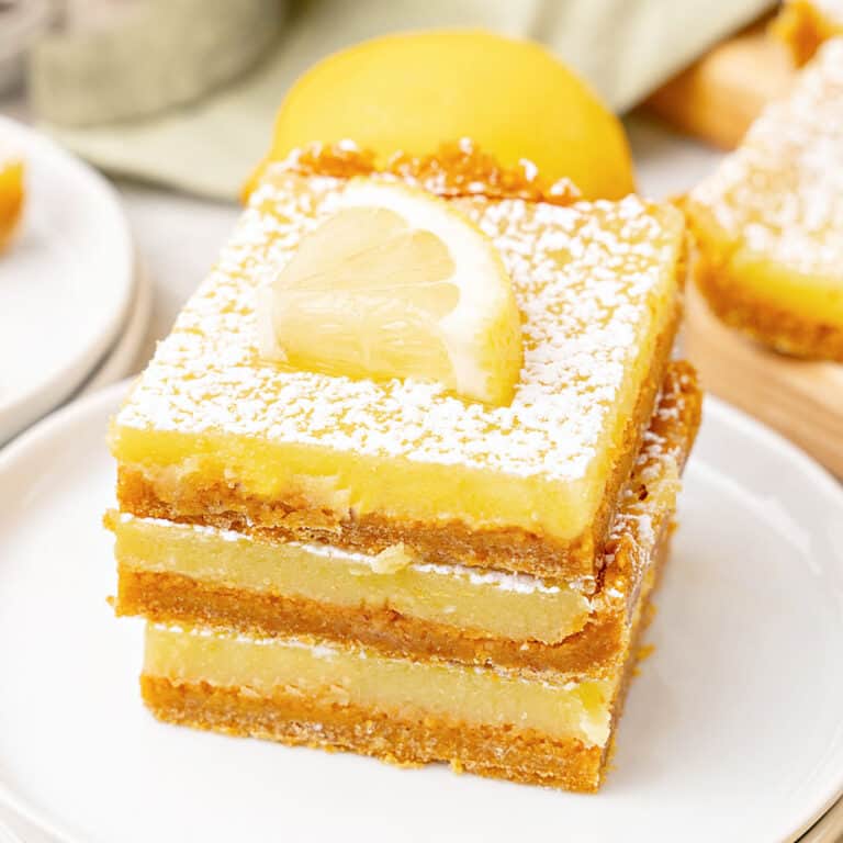 White plate with three lemon squares in a stack. Lemon slices.